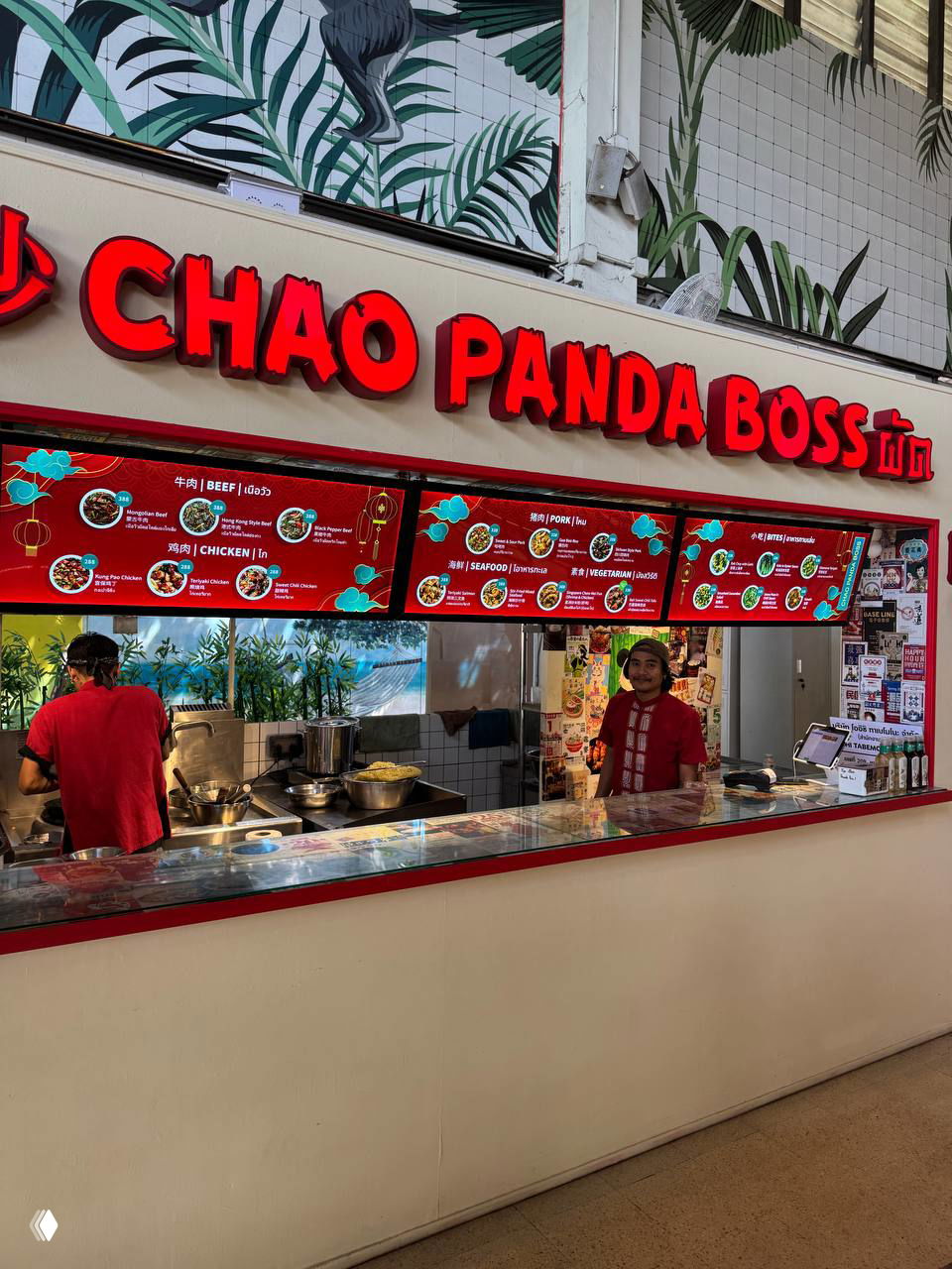 Фуд-корнер с вывеской CHAO PANDA BOSS красного цвета, стойка для приготовления лапши и электронная касса, видно оформление киоска в фуд-холе.
