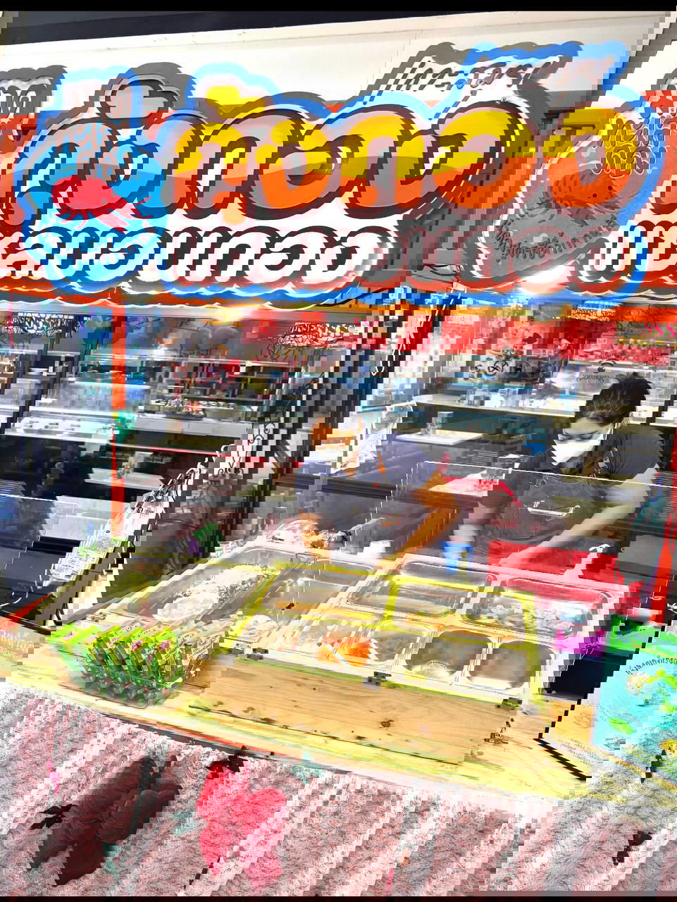 Ларёк на фудкорте: прилавок с контейнерами ингредиентов для Salmon Don, продавец в маске и яркая тайская вывеска над стойкой.