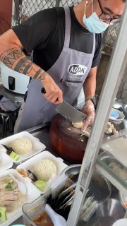 Продавец в маске и фартуке нарезает варёную курицу у большого котла — процесс подготовки мяса и нарезки в уличной точке на Ламай.