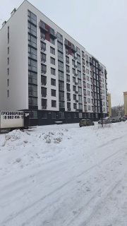 Фасад новостройки в Калининграде зимой: современный многоквартирный дом, заснеженная улица и припаркованные машины на фоне.