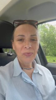 Женщина на селфи в салоне автомобиля, дневное освещение, солнцезащитные очки на голове, за окном зелёная листва и дорога.