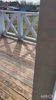 Деревянная веранда дачного дома с дощатым полом и белыми перилами, вид на участок и мягкие тени от солнца в ранний весенний день