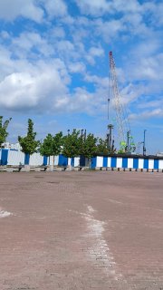Широкий план с металлическими секциями ограждения стройки ЖК Триарт, на фоне видны башенные краны, свободная площадка и небольшие деревья.