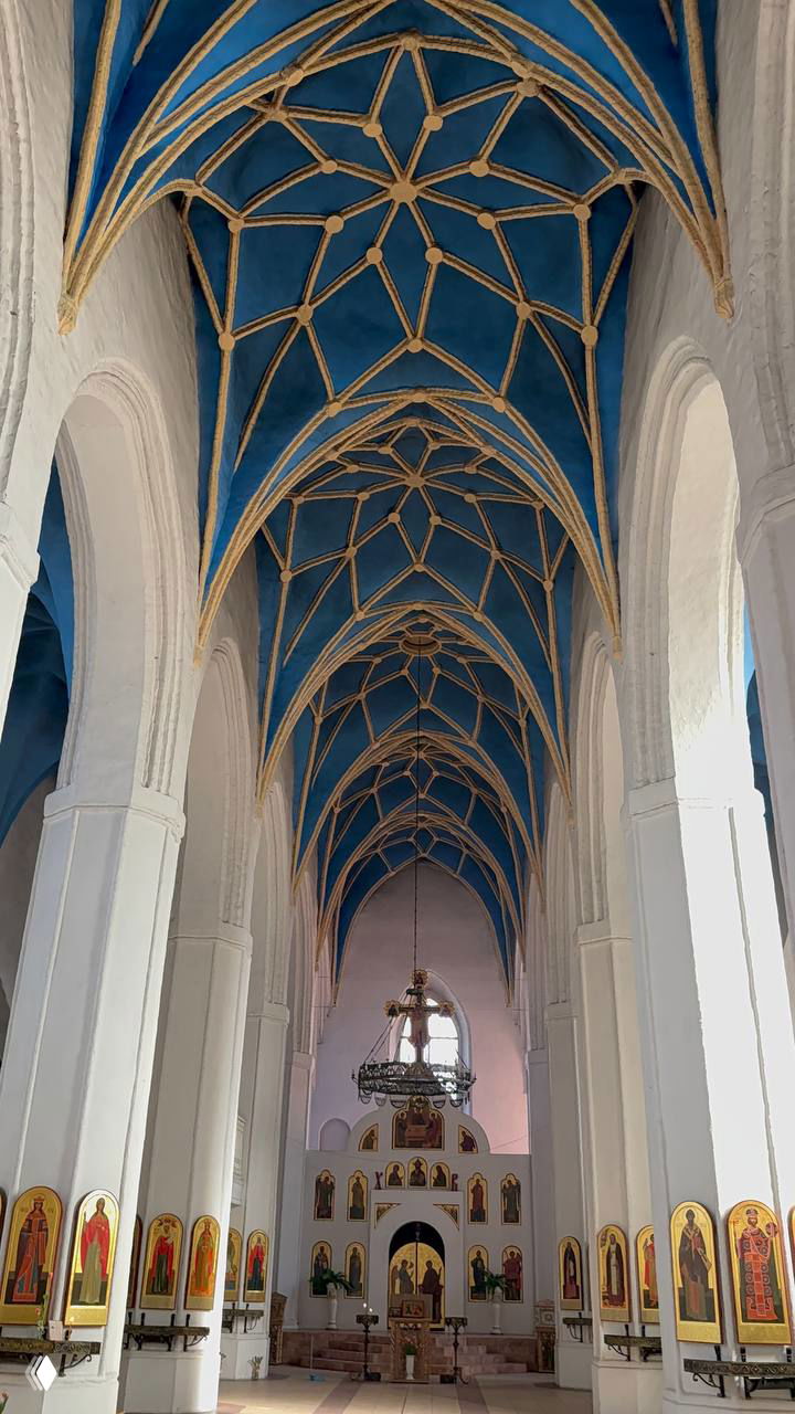 Интерьер кирхи: высокий белый неф с арочными колоннами, синие своды с золотыми ребрами и традиционный православный иконостас в алтарной части.