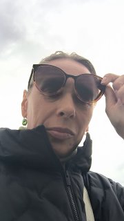 Селфи автора Ольги Дедковой на фоне неба: лицо в очках и куртке, крупный план на фоне строительного района.