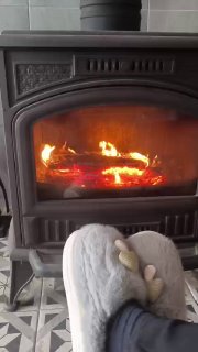 Топящаяся дровяная печь с живым пламенем, перед ней домашние тёплые тапочки — уютная сцена в дачном доме в холодный день.