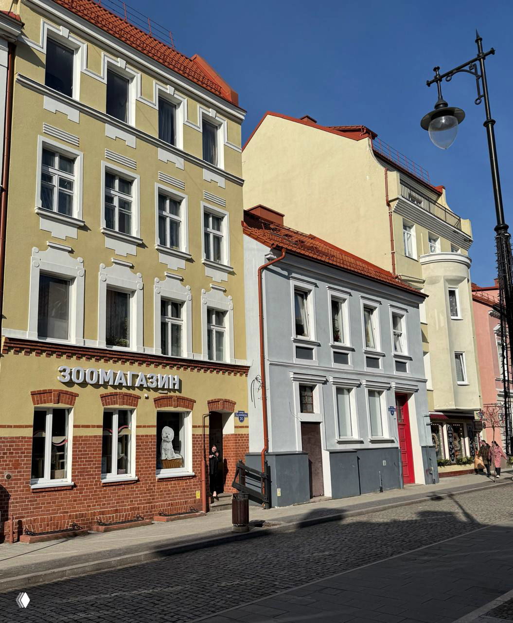 Фасады исторических немецких домов в Черняховске: нежно-жёлтые и светло-серые здания с магазинами на первом этаже и тротуаром вдоль улицы.