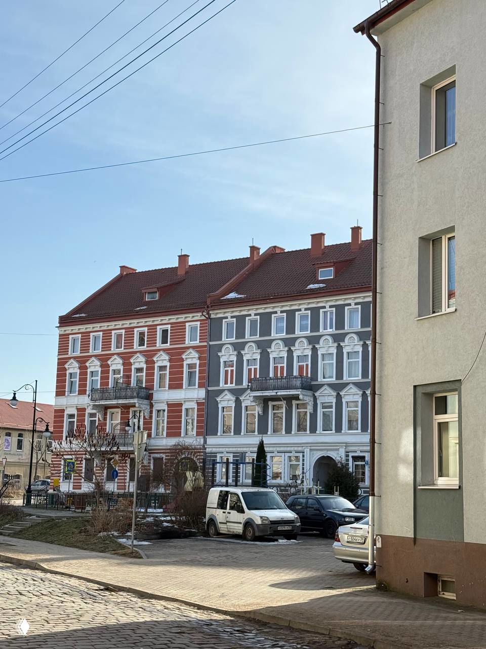 Двухцветный фасад конца XIX — начала XX века: красный и серый дома с декоративными элементами, вид с узкой улицы Черняховска.