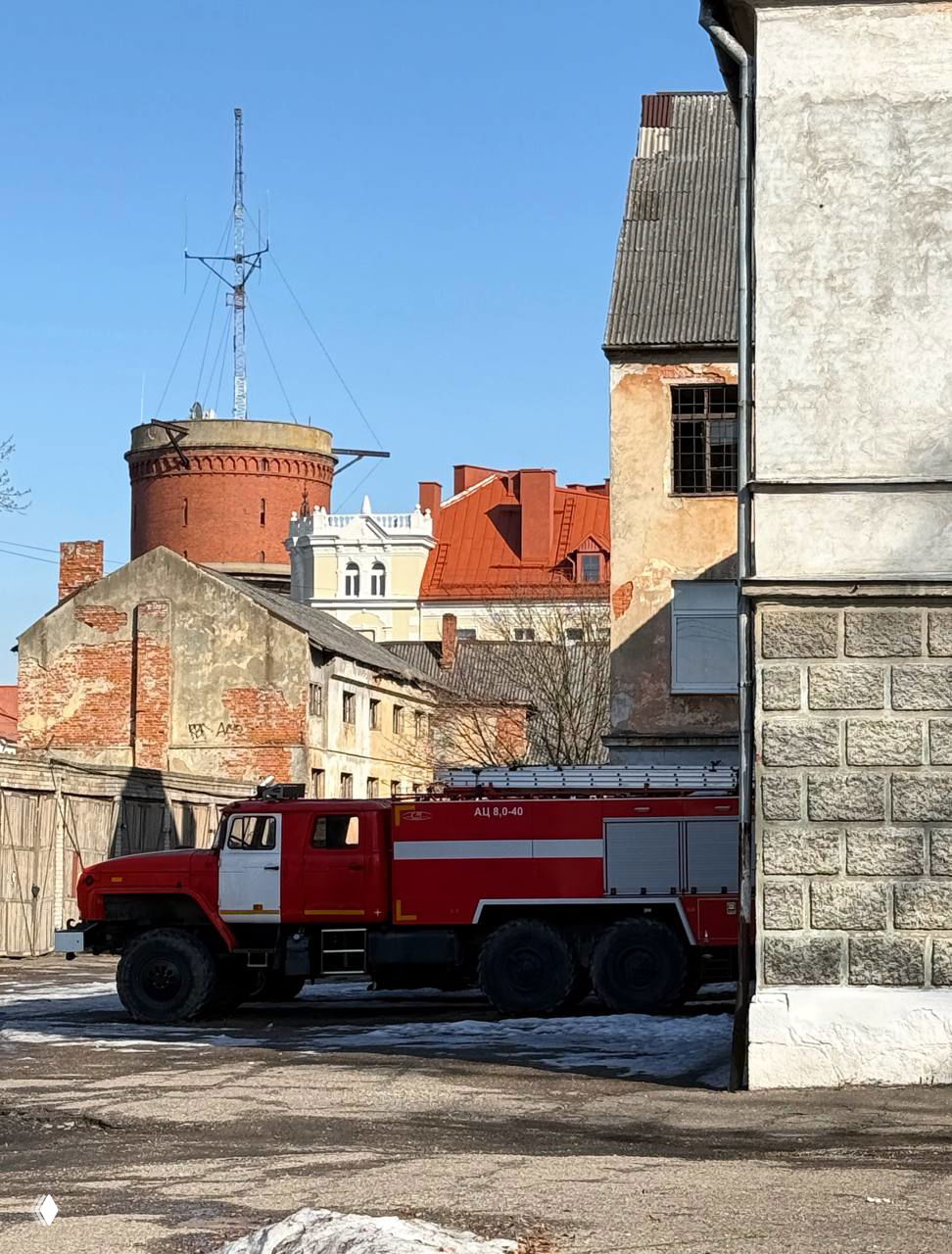 Пожарная машина на фоне разномастных зданий и старой башни в районе задних дворов Черняховска; сочетание индустриального и исторического ландшафта.