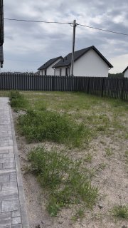 Придомовой участок в новом посёлке: неукоренившийся газон, забор по периметру и тротуарная плитка у границы участка, вид на соседние дома.