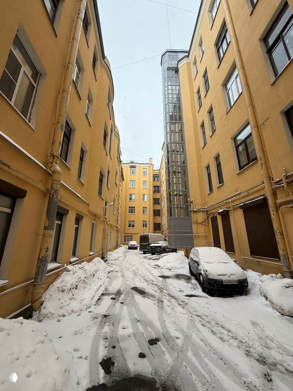 Внутренний двор доходного дома, заснеженная подъездная территория между корпусами, припаркованные машины и лифт-камера