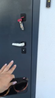 Рука у входной двери, висящие ключи в замке и часть наружной двери — кадр показывает отдельный вход в продаваемую квартиру с ключами на замлоке.