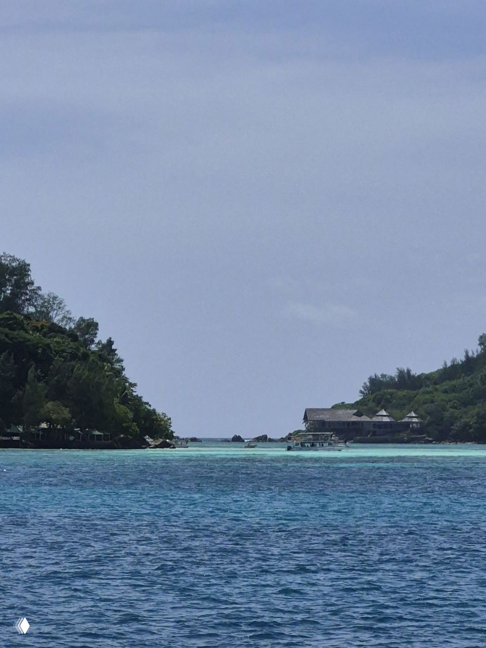Вид на лагуну и проход между островами с оттенками бирюзовой воды, рифами и несколькими прогулочными лодками у входа в бухту.