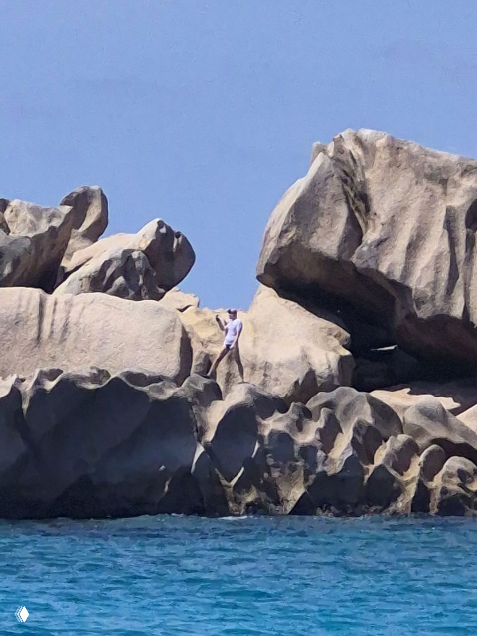 Гигантские гранитные валуны на побережье Сейшел с человеком на вершине для масштаба и бирюзовой водой у основания скал.