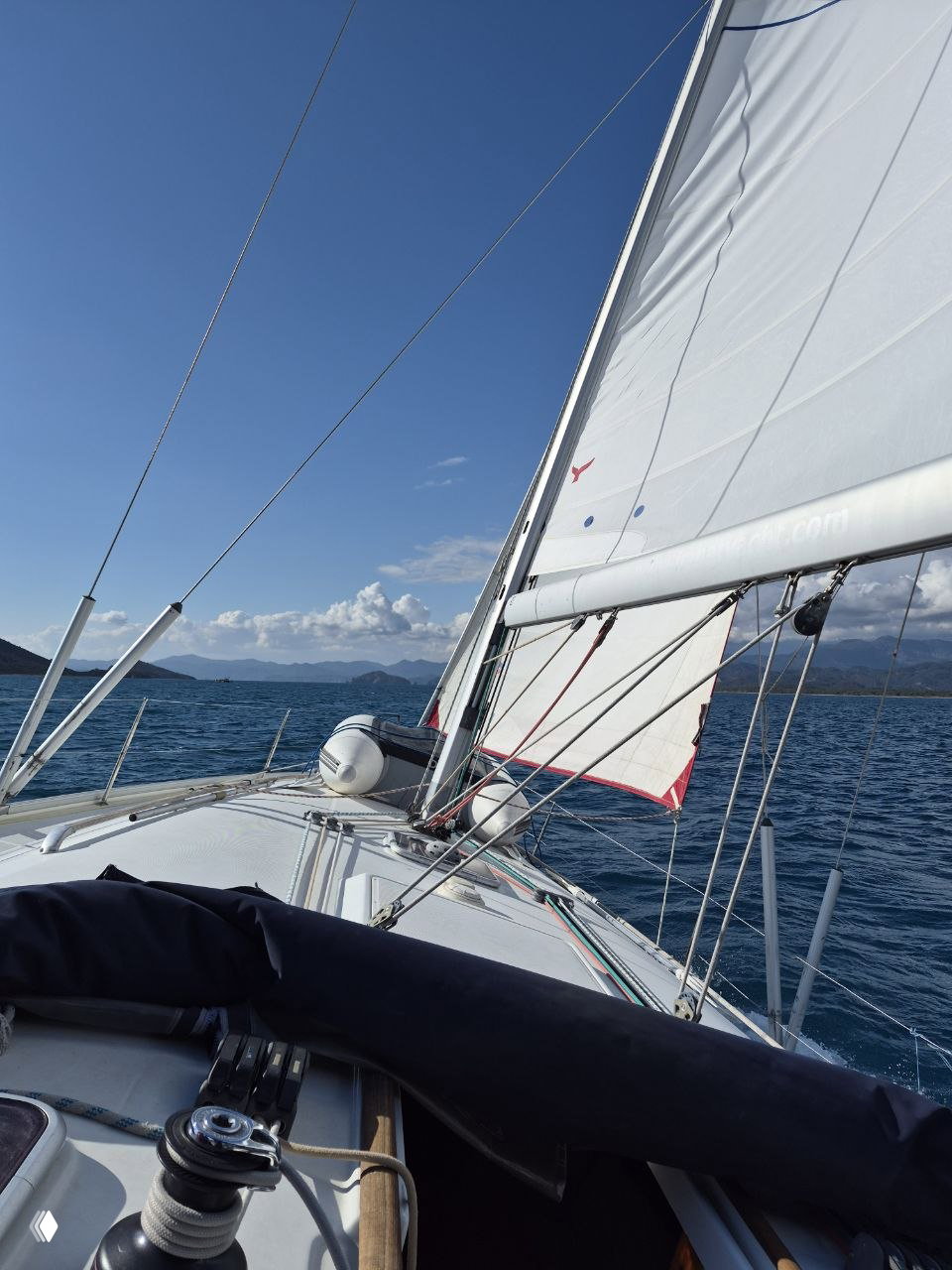 Нос яхты с поднятым парусом, море и береговой силуэт вдали при дневном ветре — вид с палубы во время практической части курса.