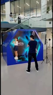 Инсталляция фотозоны «Калейдоскоп» в пространстве: шестигранная подсвеченная будка, оператор фотографирует гостя на фоне экранов и зеркал.
