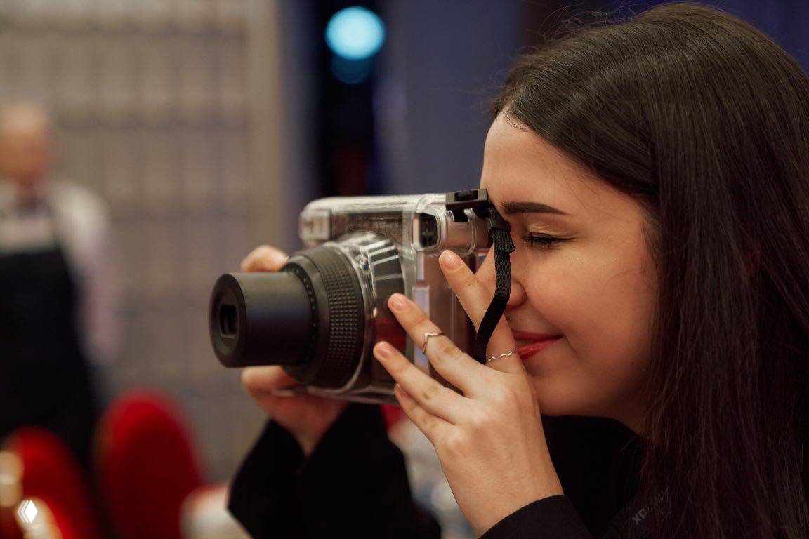 Девушка делает снимок моментальным фотоаппаратом Instax/Polaroid в интерьере мероприятия — процесс съёмки и эмоции гостей.