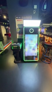 Вертикальное селфи-зеркало с яркой зелёной неоновой подсветкой по контуру, верхней световой панелью и отдельным принтером слева на событии в тёмном зале.