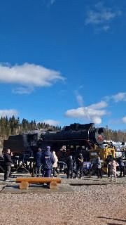 Посетители у большого паровоза на территории Горного парка Рускеала: толпа вокруг ретро‑локомотива на фоне синего неба и паркового пространства.