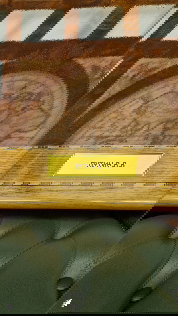 Кожаное кресло с табличкой «ПУТИН В.В.» и отображением старой карты на деревянной поверхности внутри зала Русского географического общества.