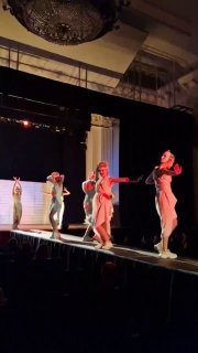 Небольшой фрагмент сценического действия с несколькими актрисами, акцент на движении и линиях костюмов в светлом оформлении.