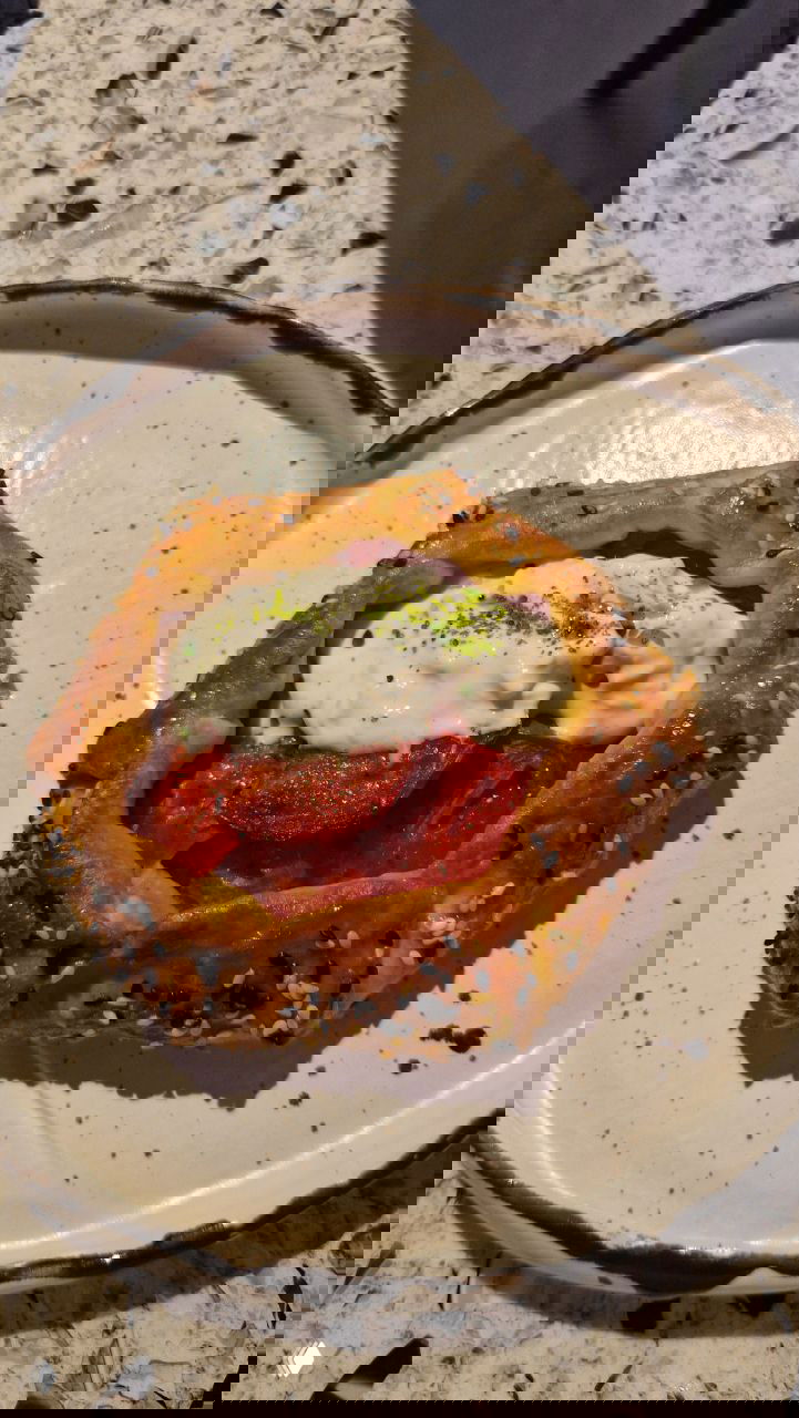 Галета с томатами на белой тарелке: золотистая хрустящая корочка, томаты и сверху сливочно-йогуртовый соус — поданная закуска из ужина в FLØR.