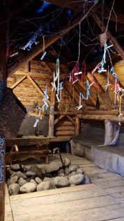 Интерьер жилища викингов с подвешенными амулетами и элементами быта; деревянный пол, очаг и декоративные детали в тёплом свете.