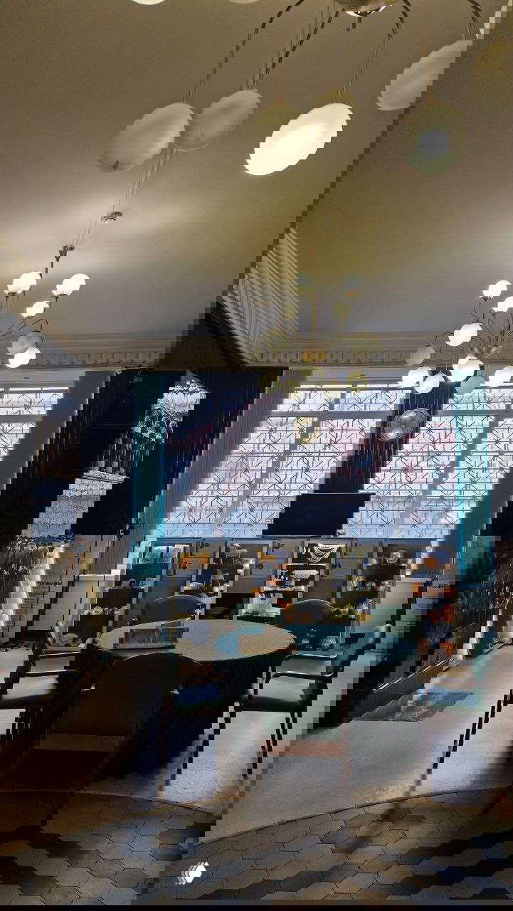 Меблированный зал с круглым столом, люстрой и печной плитой — обстановка первого этажа, где проходят экскурсии по банку в Сортавале.