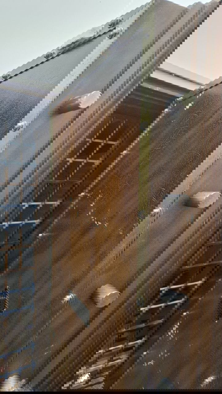 Массивная дверь банковского хранилища с выступающими ригелями и металлическими элементами — крупный план механизма старого сейфа в экспозиции.