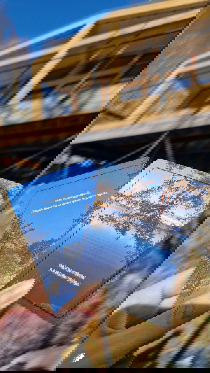 Рука держит две приветственные карточки парка‑отеля на фоне размытых деревянных домиков и приоткрытой террасы — атмосфера отдыха.