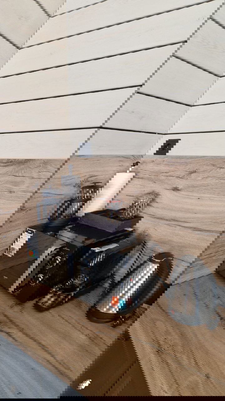 Мини‑кухня в домике: микроволновка, кофемашина, капсулы и электрический чайник на деревянной столешнице.