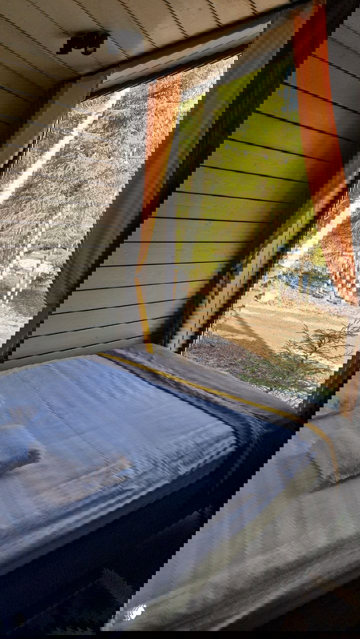 Интерьер спальни с кроватью у панорамного окна и видом на лес, светлый декор и уютная постель в домике парка‑отеля.