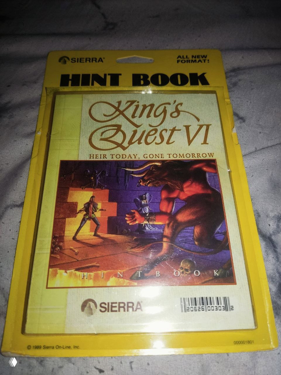 Фронтальная фотография официального hint book для King's Quest VI в жёлтой блистерной упаковке с логотипом Sierra и оформлением обложки игры.