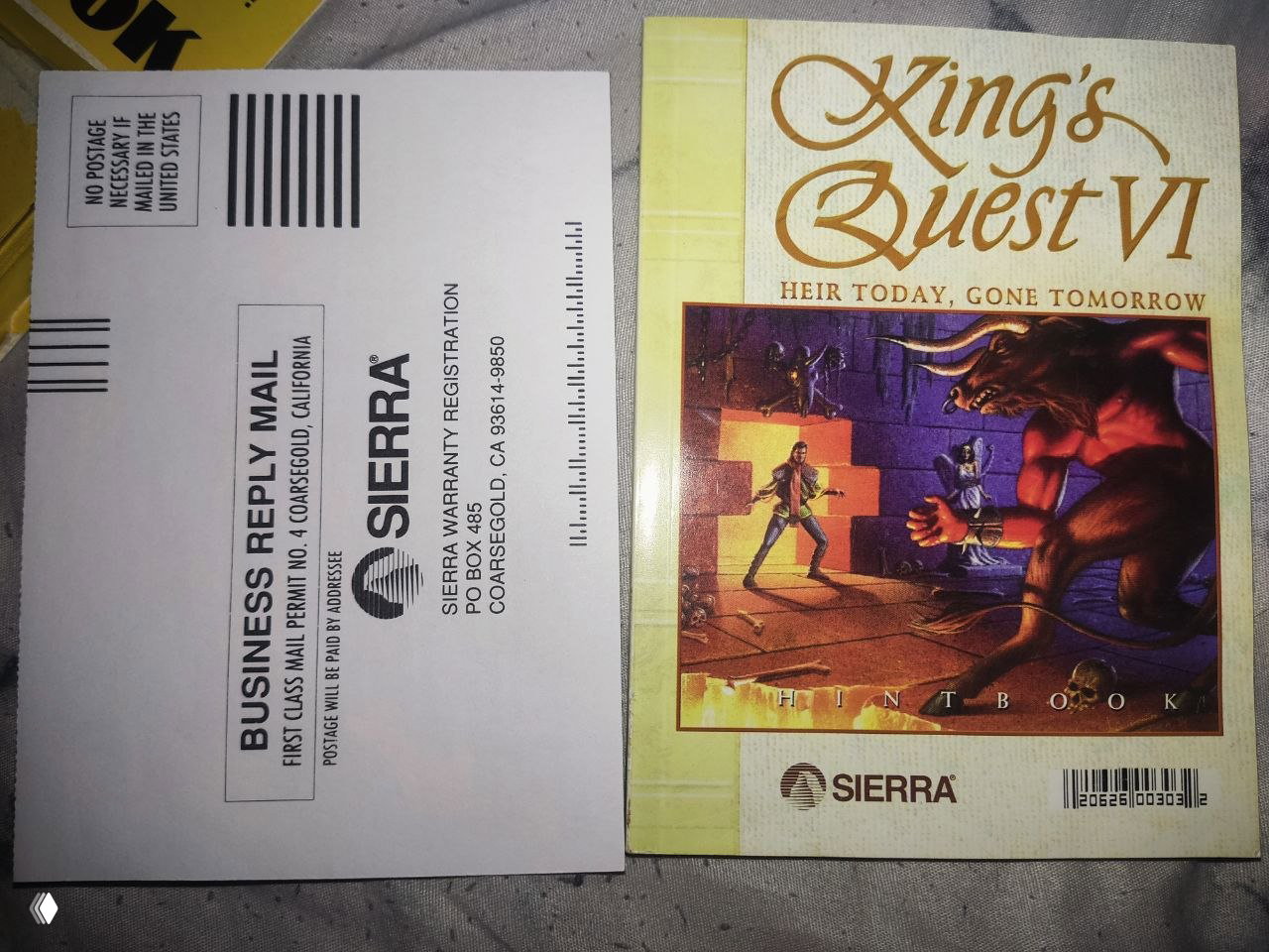 Книжка подсказок King's Quest VI рядом с почтовой регкартой Sierra — вид спереди, показывающий обложку и упаковочный конверт регистрации.