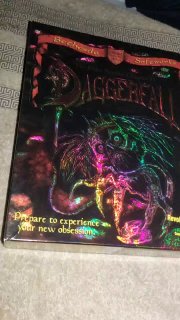 Вертикальное фото коробки Daggerfall с сильными переливами фольги под разным освещением; наблюдаются голографические оттенки и детальное оформление лицевой стороны.
