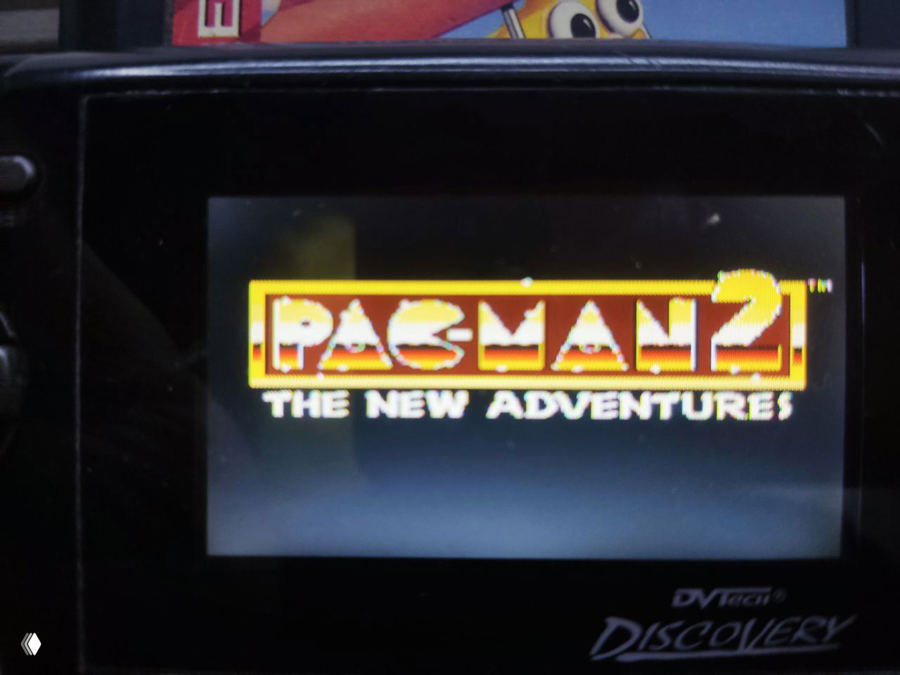 Заставка игры Pac‑Man 2 на экране портативного устройства Discovery: логотип The New Adventures на тёмном фоне, картридж успешно стартовал.