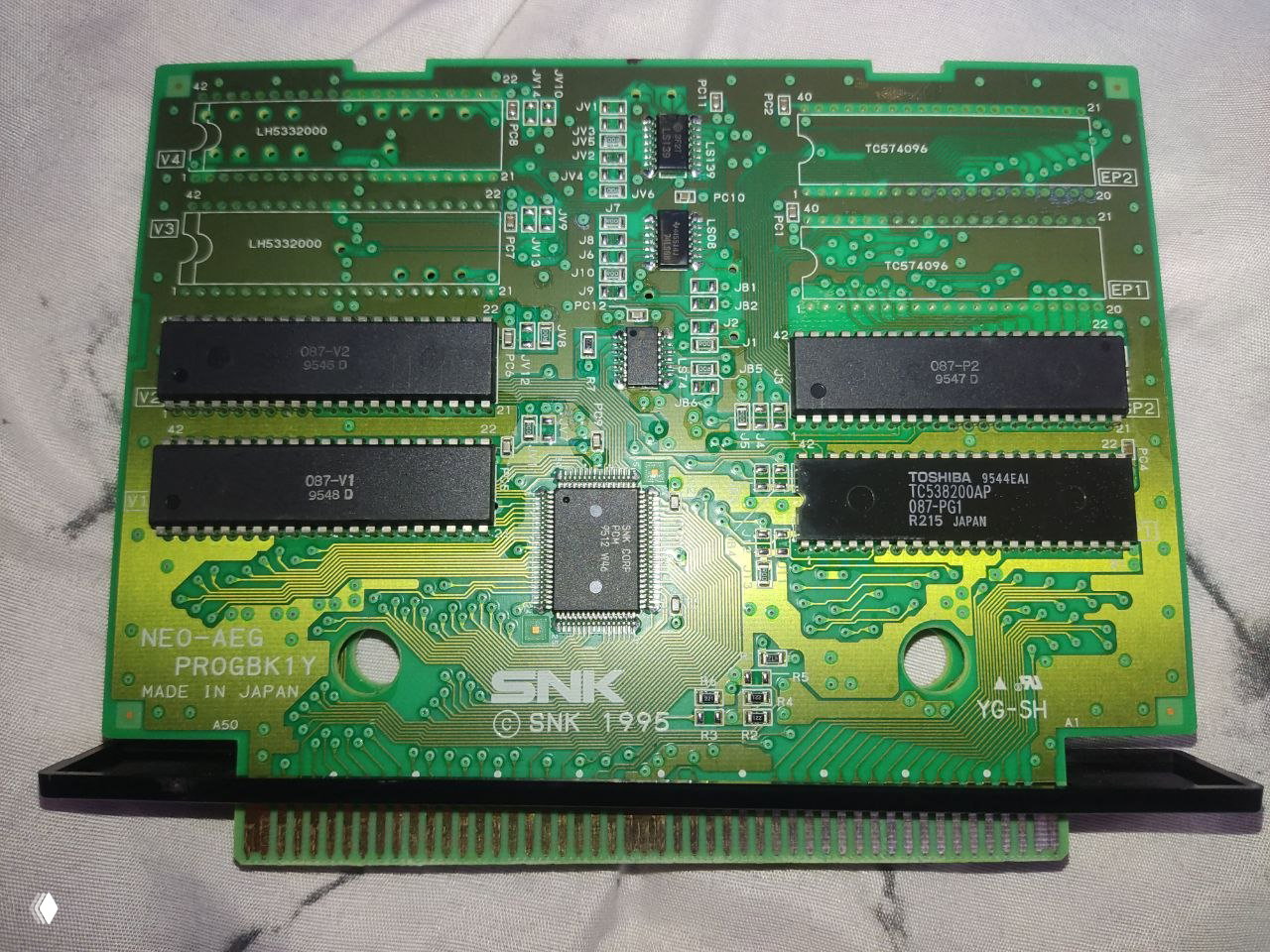Печатная плата Neo·Geo AES с микросхемами и маркировкой SNK, видны контакты и надписи NEO-AEG PROGBK1Y, изображение платы крупным планом.