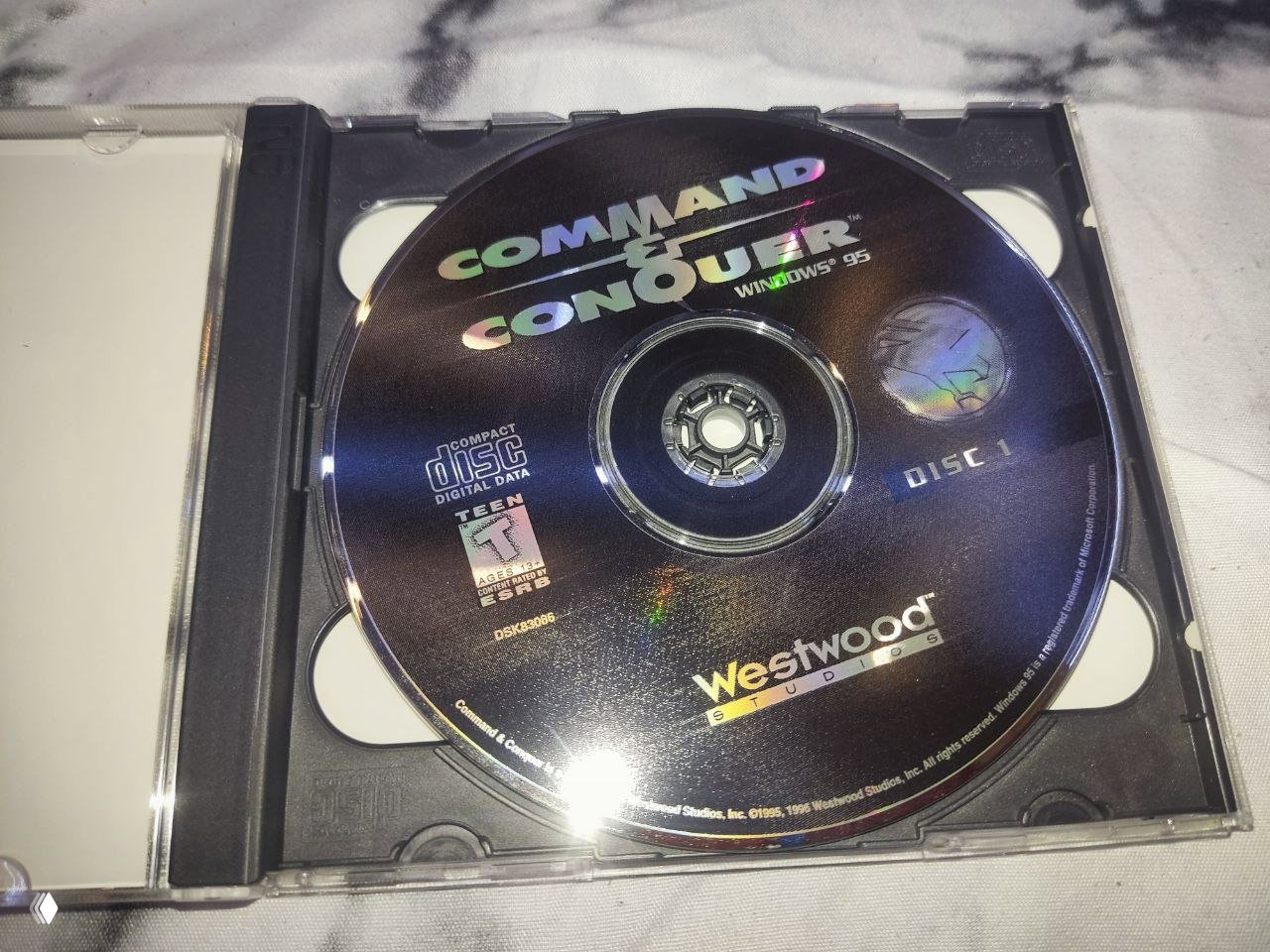 Крупный план диска Command & Conquer в джевеле: голографическая маркировка, надписи Westwood и Disc 1, видны отражения света.