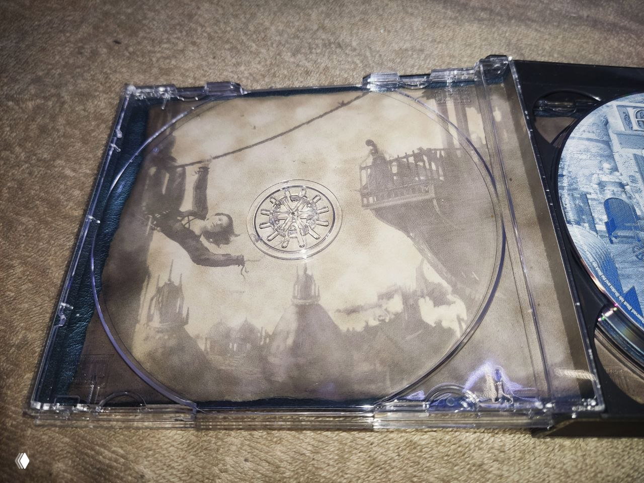 Крупный план внутренней стороны джевел‑коробки с сепийной иллюстрацией города и фигурой на балконе; видна прозрачная посадочная зона диска и графика внутри кейса.