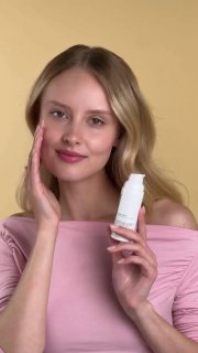 Женщина демонстрирует флакон увлажняющей сыворотки Loved by You на светлом нейтральном фоне — видна упаковка, форма и размер флакона.