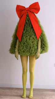 Креативный кадр: человек в зелёном пушистом костюме-ёлке с большим красным бантом, позирует на светлом нейтральном фоне, иллюстрация праздничной темы поста