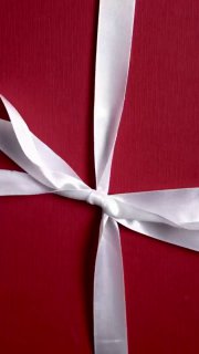 Красная подарочная упаковка с белой атласной лентой крупным планом, аккуратно перевязанная, символ новогодней акции и подарка бренда