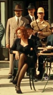 Ретро-кадр на уличном кафе: женщина в чёрном платье и чулках сидит за столиком, на заднем плане мужчины в костюмах и шляпах — атмосфера старого города.