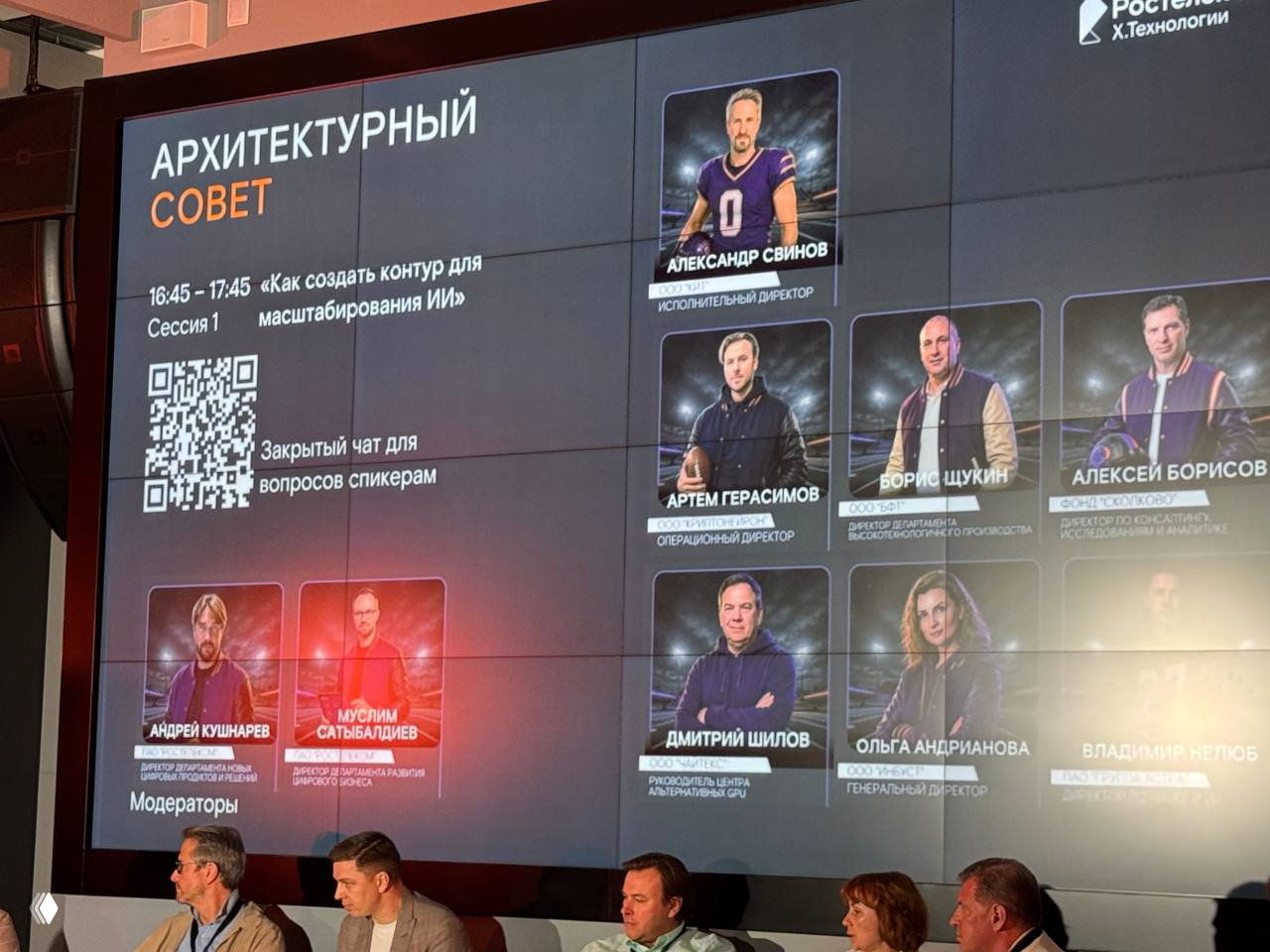Крупный экран с слайдами и карточками спикеров, на переднем плане часть сцены и участник с микрофоном, видны детали презентации архитектурного совета.