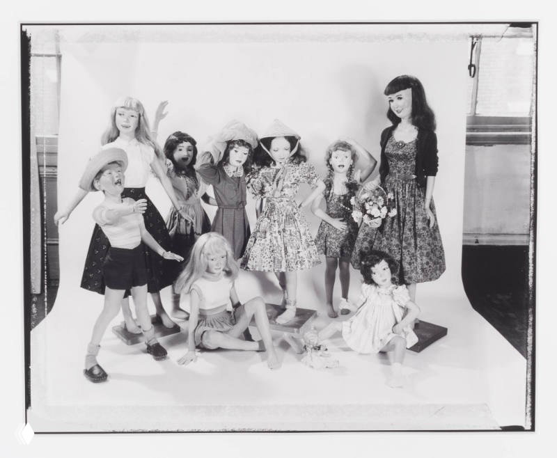 Чёрно‑белая студийная фотография группы реалистичных кукол Мортона Бартлетта в антрактах постановки — разные росты, одежда и позы.