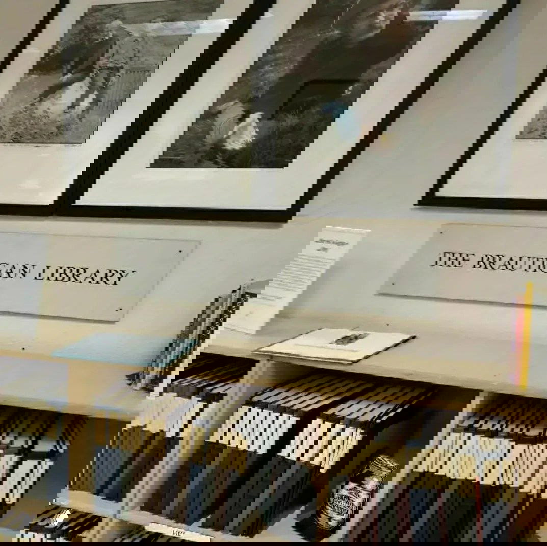 Полка с подписанными рукописями и табличкой «THE BRAUTIGAN LIBRARY», на стене надпись и оформленные фотографии; на полке видна декоративная банка майонеза.