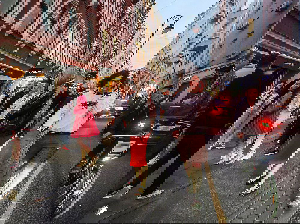 Оживлённая пешеходная улица с толпой людей, прохожие и велосипедист на асфальтовой городской магистрали в вечернем свете.