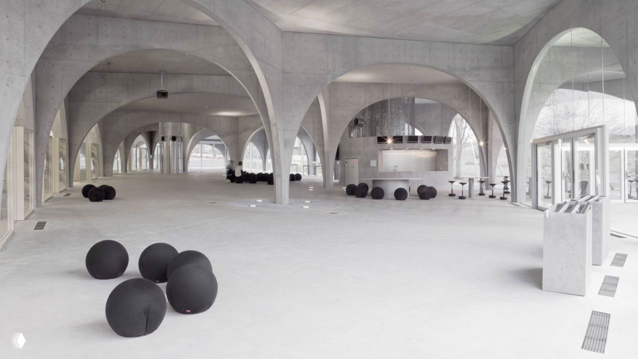 Просторный первый уровень библиотеки с бетонными арками, минимальной мебелью и свободной планировкой для выставок и мероприятий.