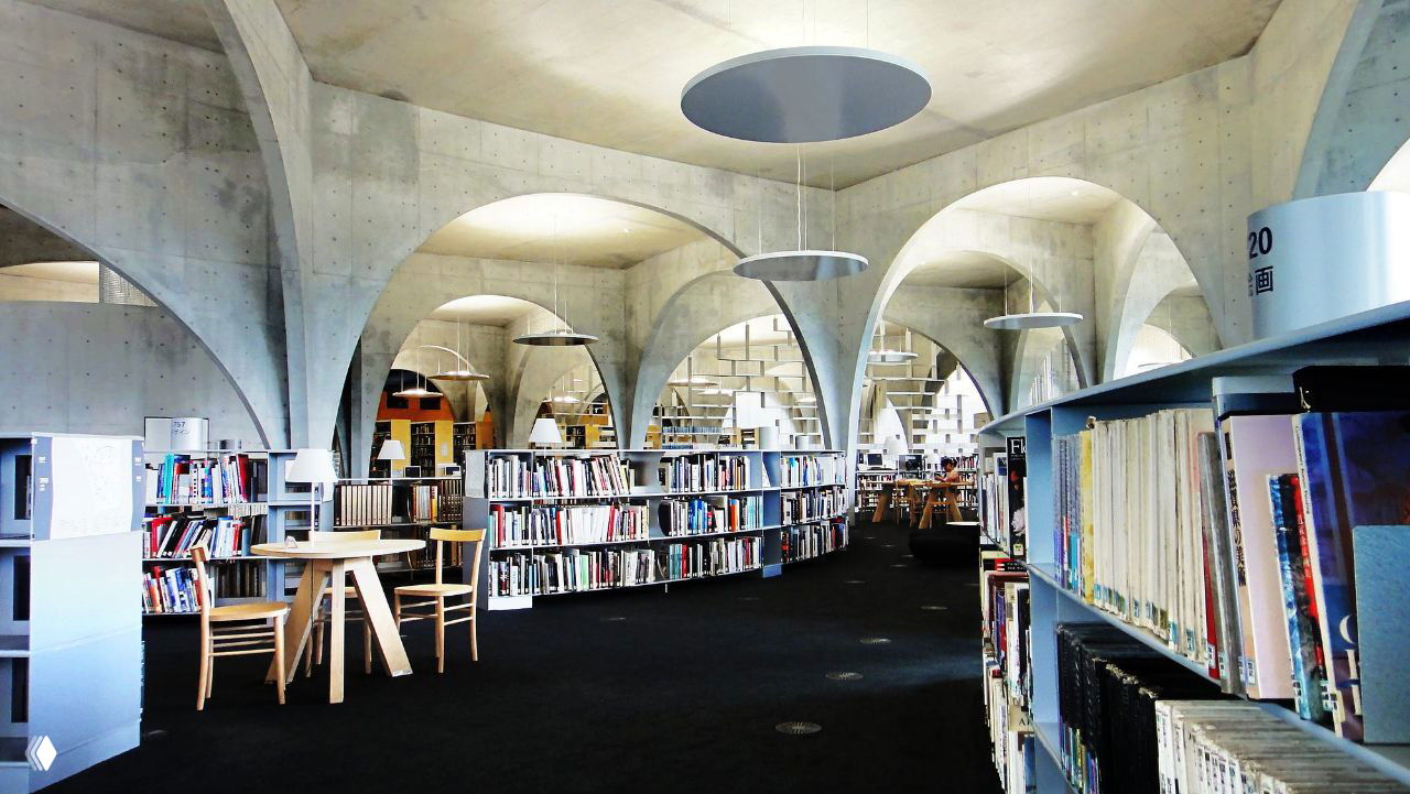 Полукруглые проходы между книжными стеллажами и арками внутри библиотеки Тама: сочетание функциональности и скульптурной структуры пространства.