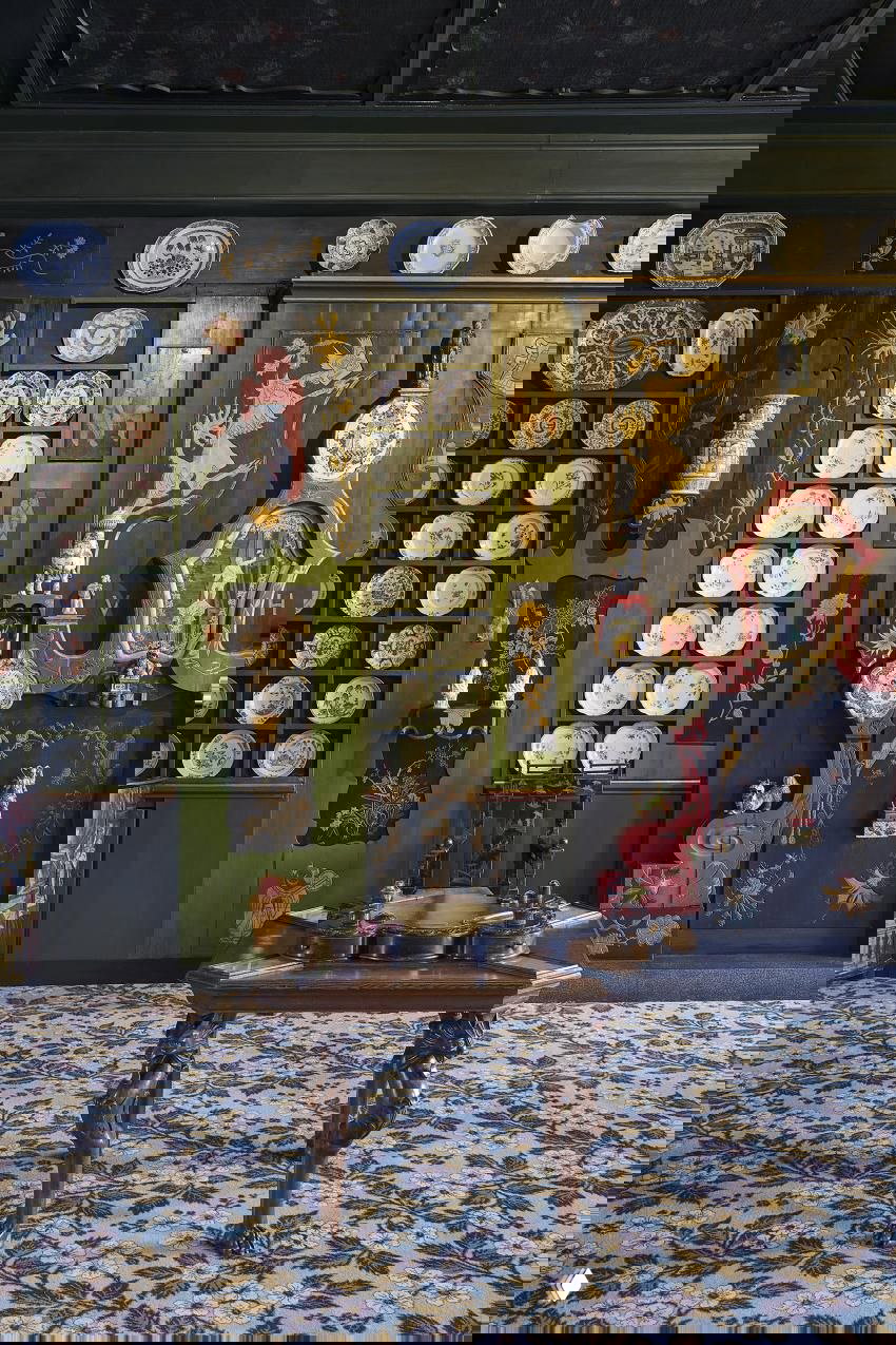 Крупный план стены с декоративными тарелками и маленьким резным столиком на узорчатом ковре в одном из залов дома Виктора Гюго, детали экспозиций.